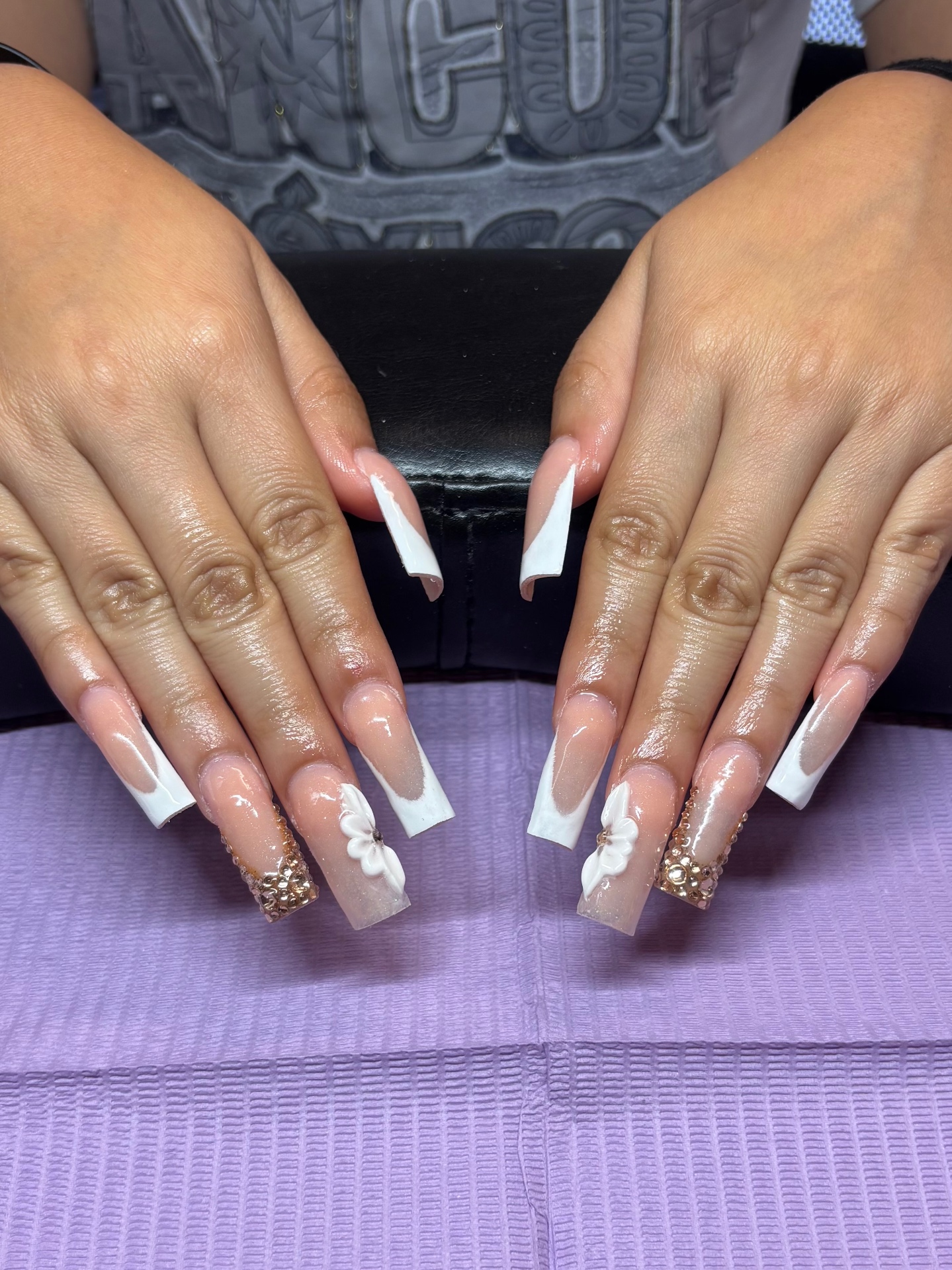 Nude nails with white French tips, 3D floral art, and rose gold crystal accents